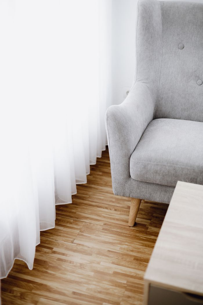 Minimalist living room with a gray armchair, sheer curtains, and wooden flooring.